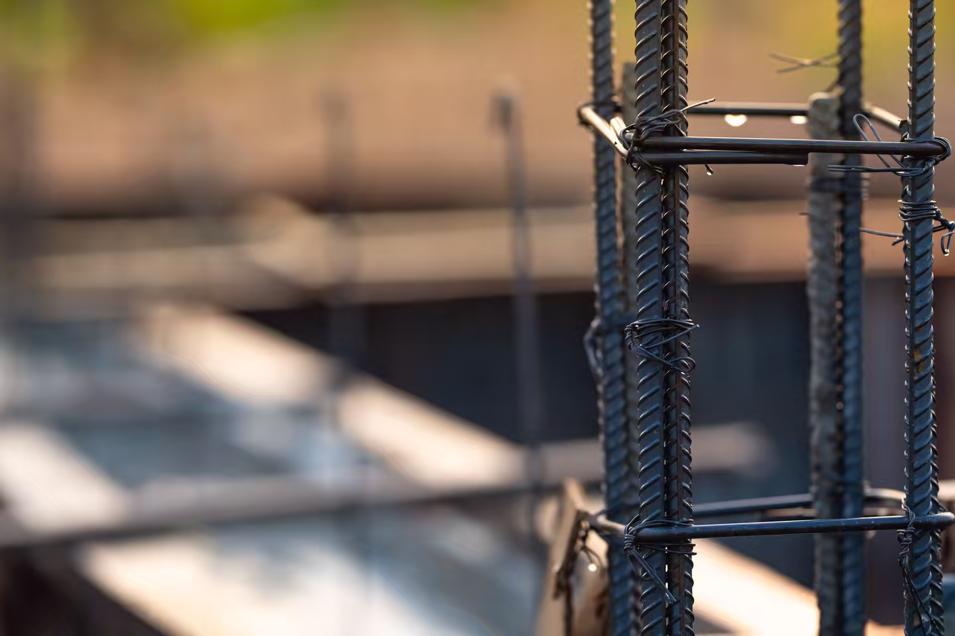 Steel reinforcement cage tied with wire on a construction site, with concrete formwork blurred behind