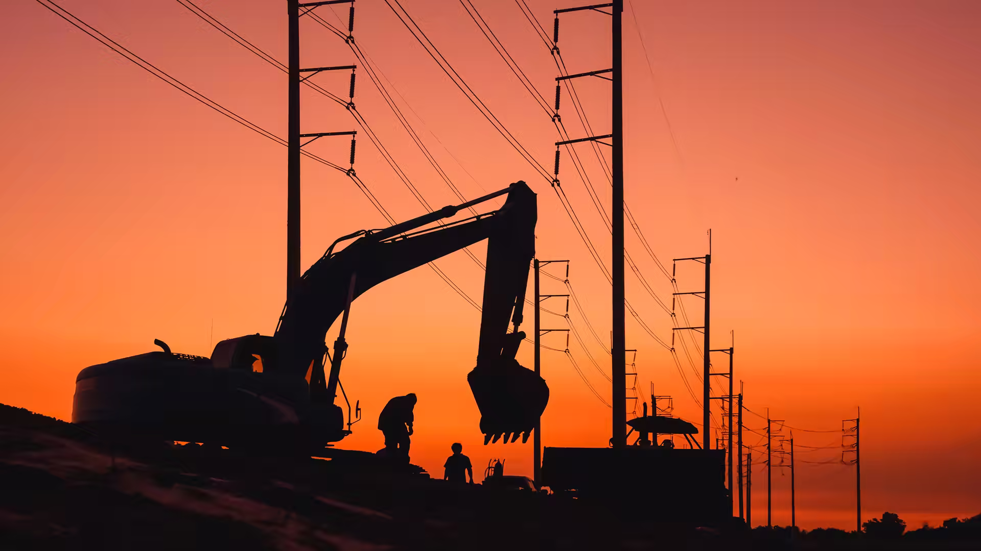 Excavator and haul truck silhouetted against a dusk sky on a worked site