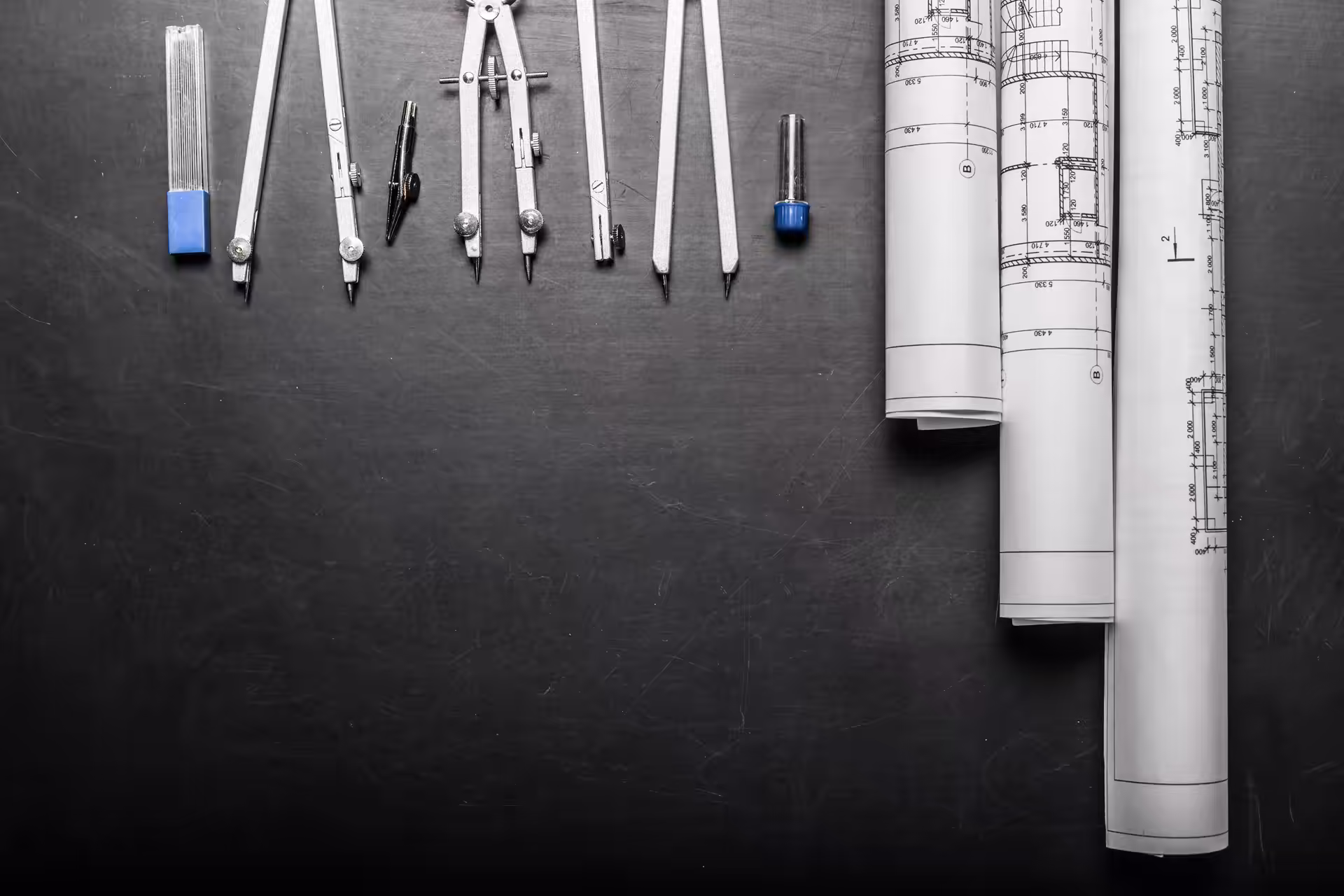 Drafting instruments and rolled technical drawings laid on a dark desk