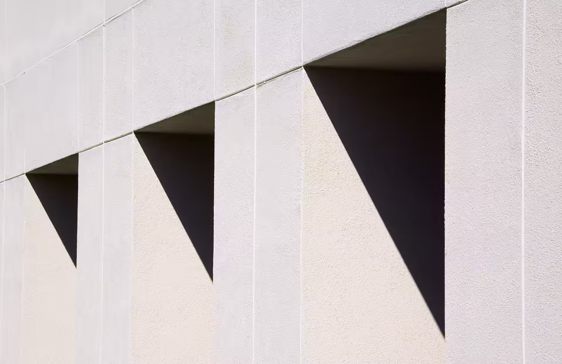 Angular triangular shadows falling across a pale concrete facade